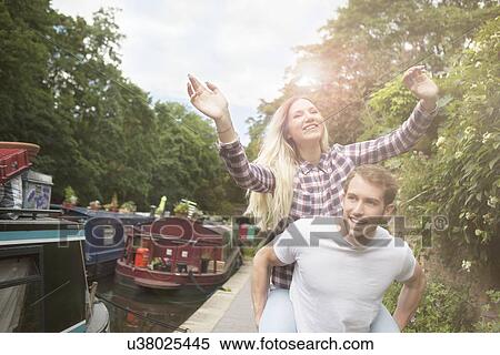 Stock Photography - Couple playing piggyback by canal, East London, UK. Fotosearch