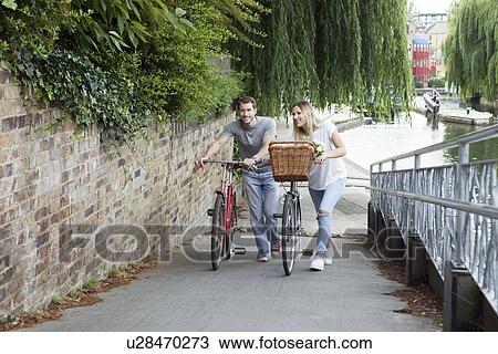 Stock Image - Cyclist couple pushing bike along canal, London, UK. Fotosearch