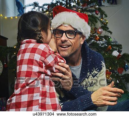 Daughter whispering to father in santa hat at christmas View Large Photo Image Picture - Daughter whispering to father in santa hat at christmas. Fotosearch