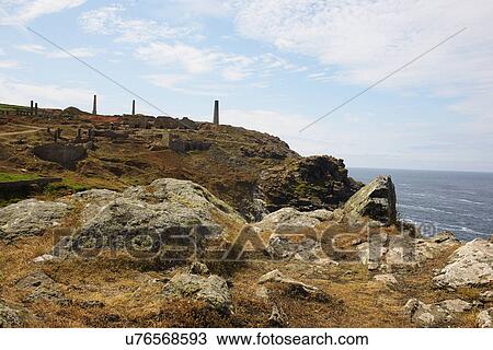 Stock Image - Distant view of tin mine chimneys on coastal path, Trewellard, Penzance, Cornwall, UK. Fotosearch