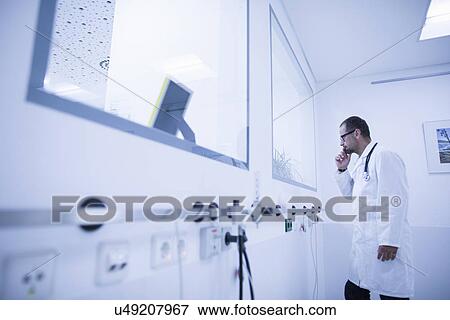 Doctor watching through treatment room window in hospital View Large Photo Image Stock Photo - Doctor watching through treatment room window in hospital. Fotosearch