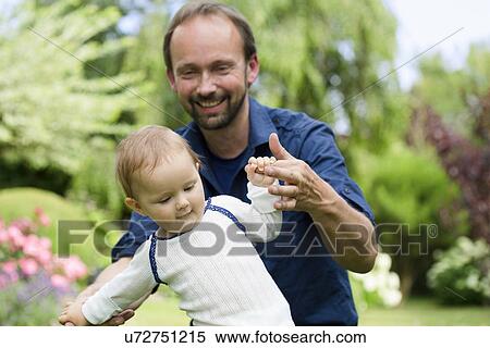 Stock Photography - Father holding baby daughters hands whilst toddling. Fotosearch