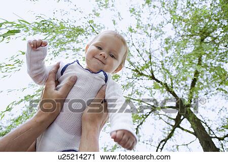 Stock Image - Father holding up baby daughter in garden. Fotosearch
