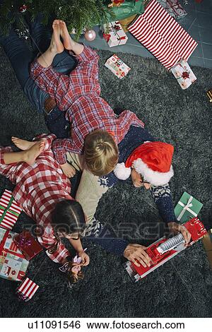 Stock Photograph - Father lying on sitting room floor opening christmas gifts with daughter and son. Fotosearch