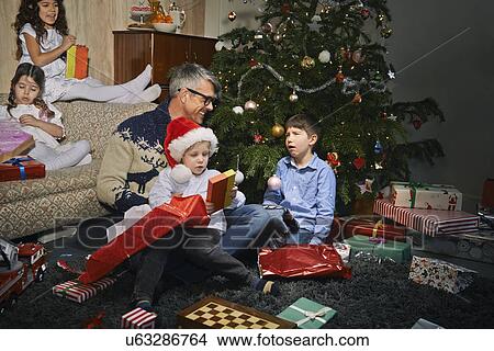 Father on sitting room floor opening christmas gifts with children View Large Photo Image Picture - Father on sitting room floor opening christmas gifts with children. Fotosearch