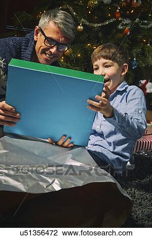 Stock Image - Father on sitting room floor opening christmas gifts with son. Fotosearch