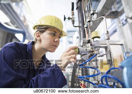 Stock Image - Female engineer checking cables on industrial machinery. Fotosearch