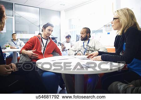 Stock Image - Female lecturer and a group of college students having informal discussion in classroom. Fotosearch