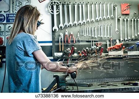 Stock Photograph - Female mechanic grinding metal in workshop. Fotosearch