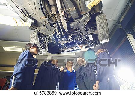Stock Photo - Five college students looking up from beneath car in garage workshop. Fotosearch