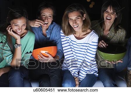 Four women laughing and watching TV with snack bowls View Large Photo Image Stock Image - Four women laughing and watching TV with snack bowls. Fotosearch