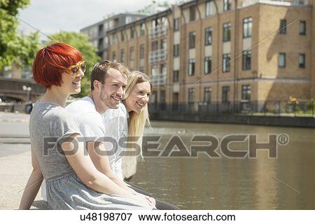 Stock Photo - Friends sitting on canal side, East London, UK. Fotosearch