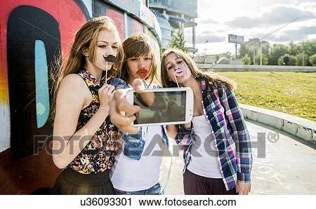 Friends taking selfie wearing fake lips and moustache, mural in background View Large Photo Image Stock Image - Friends taking selfie wearing fake lips and moustache, mural in background. Fotosearch