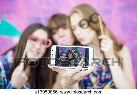 Stock Photograph - Friends taking selfie wearing fake spectacles and lips. Fotosearch