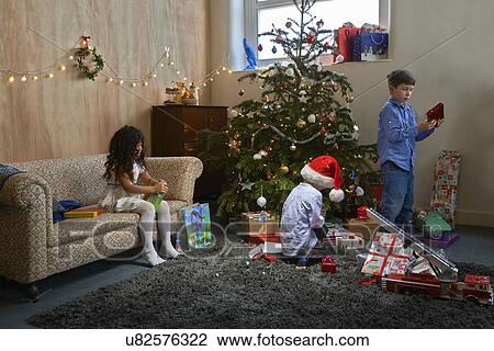 Stock Image - Girl and two brothers opening christmas gifts in sitting room. Fotosearch