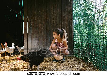 Stock Image - Girl in barn with hens. Fotosearch
