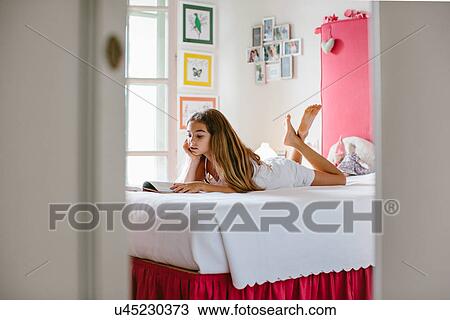 Stock Image - Girl lying on bed, reading. Fotosearch