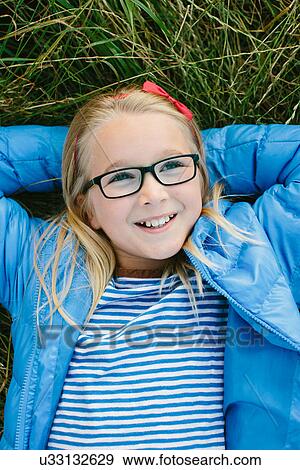 Girl lying on grass wearing glasses, daydreaming View Large Photo Image Stock Photo - Girl lying on grass wearing glasses, daydreaming. Fotosearch