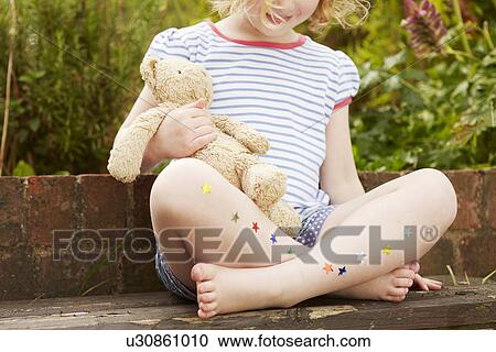 Stock Image - Girl on garden seat with star stickers on legs. Fotosearch