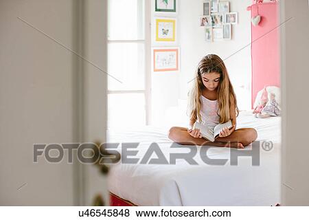 Stock Photo - Girl sitting on bed, reading book. Fotosearch