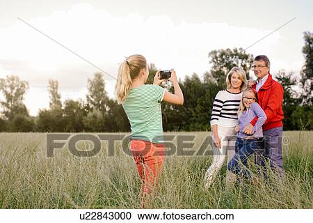 Stock Image - Granddaughter photographing grandparents and sister in field. Fotosearch