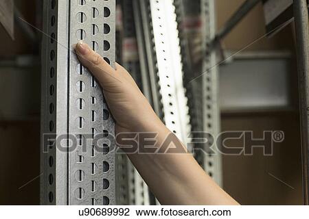 Stock Image - Hand of female customer selecting metal bars in hardware store. Fotosearch