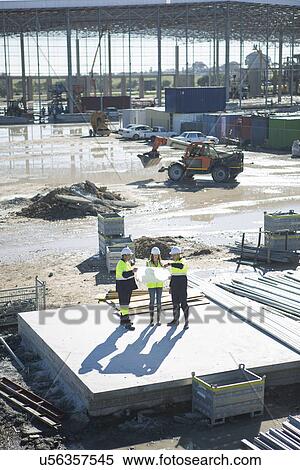 Stock Photography - High angle view of architects and site manager looking at blueprint on construction site. Fotosearch