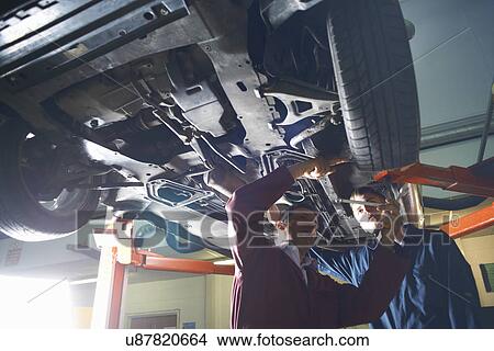 Picture - Lecturer demonstrating to male student below car in college garage. Fotosearch