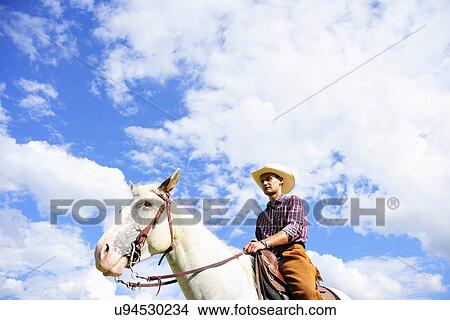 Low angle portrait of young man in cowboy gear riding horse View Large Photo Image Picture - Low angle portrait of young man in cowboy gear riding horse. Fotosearch