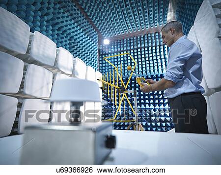 Stock Photograph - Low angle view of scientist preparing to measure electromagnetic waves in anechoic chamber. Fotosearch
