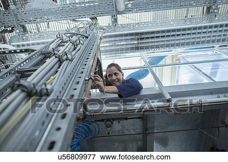 Stock Photo - Low angle view of smiling female engineer examining cables in factory. Fotosearch