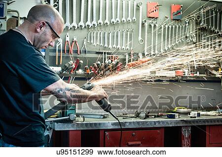 Stock Photo - Male mechanic grinding metal in workshop. Fotosearch