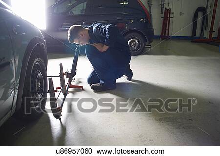 Stock Image - Male student mechanic checking car wheel in college garage. Fotosearch