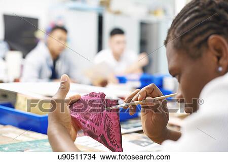 Picture - Male student painting on swatch of fabric in textile class. Fotosearch