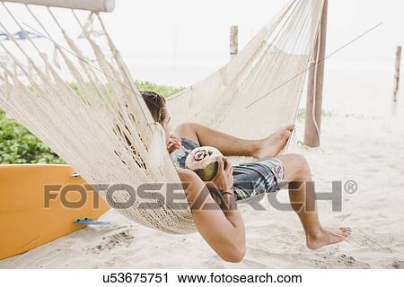 Man enjoying coconut water in hammock on beach View Large Photo Image Stock Image - Man enjoying coconut water in hammock on beach. Fotosearch