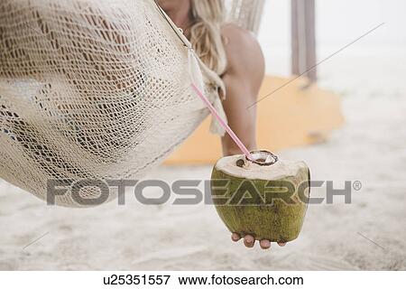 Stock Photo - Man enjoying coconut water in hammock on beach. Fotosearch