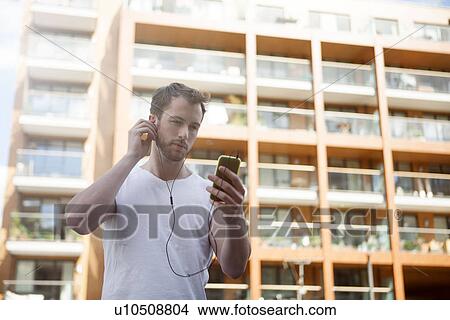 Man listening to music on headphones, building in background View Large Photo Image Picture - Man listening to music on headphones, building in background. Fotosearch