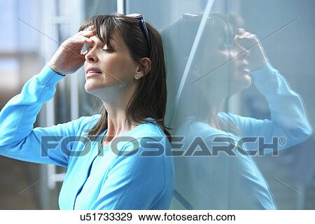 Mature businesswoman leaning against glass wall in office with hand on face View Large Photo Image Stock Photo - Mature businesswoman leaning against glass wall in office with hand on face. Fotosearch