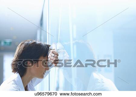 Stock Image - Mature businesswoman with eyes closed leaning against glass wall in office. Fotosearch