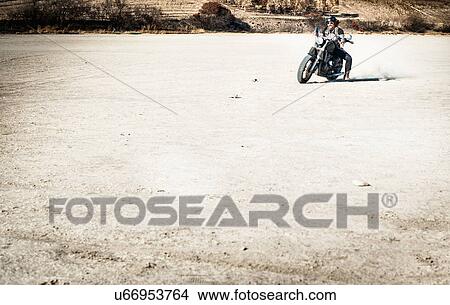 Picture - Mature man riding motorcycle on arid plain, Cagliari, Sardinia, Italy. Fotosearch