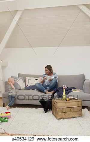 Stock Photo - Mature mother drinking coffee with attention seeking baby daughter. Fotosearch
