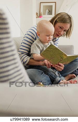 Stock Photo - Mature mother reading storybook to baby daughter on sitting room sofa. Fotosearch