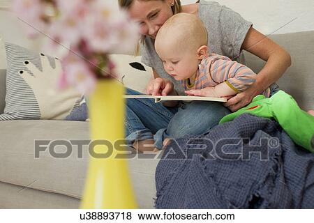 Mature mother reading to baby daughter on sitting room sofa View Large Photo Image Stock Photo - Mature mother reading to baby daughter on sitting room sofa. Fotosearch