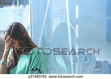 Mid adult businesswoman leaning against glass wall in office with hand on face View Large Photo Image Picture - Mid adult businesswoman leaning against glass wall in office with hand on face. Fotosearch