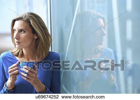 Mid adult businesswoman leaning against glass wall in office with cup of coffee View Large Photo Image Stock Image - Mid adult businesswoman leaning against glass wall in office with cup of coffee. Fotosearch