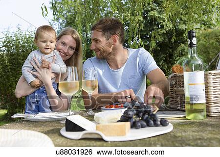 Stock Photograph - Mid adult couple and baby daughter sitting at picnic table in garden. Fotosearch