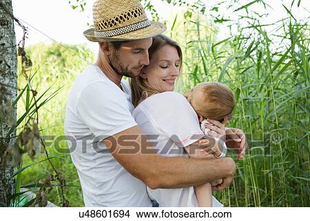 Picture - Mid adult couple and baby daughter with arms around each other in reeds. Fotosearch