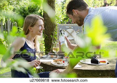 Stock Photo - Mid adult couple having picnic with white wine in garden. Fotosearch