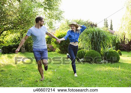 Picture - Mid adult couple holding hands whilst running in garden. Fotosearch