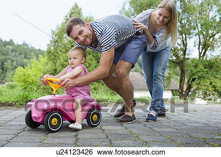 Mid adult couple pushing baby daughter on toy car in garden View Large Photo Image Stock Photograph - Mid adult couple pushing baby daughter on toy car in garden. Fotosearch